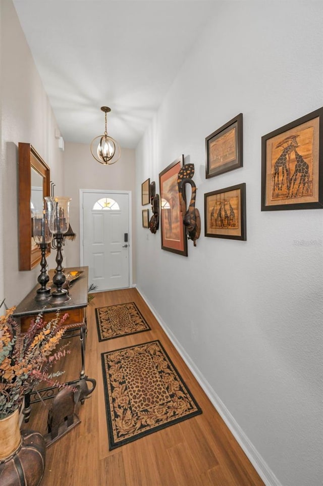 doorway to outside with a notable chandelier, baseboards, and wood finished floors