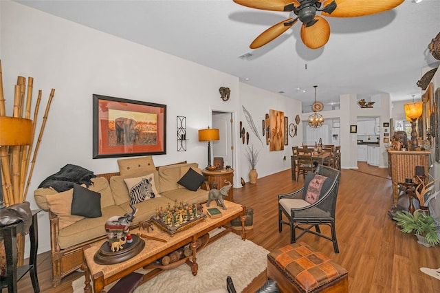 living room featuring ceiling fan with notable chandelier, visible vents, and wood finished floors