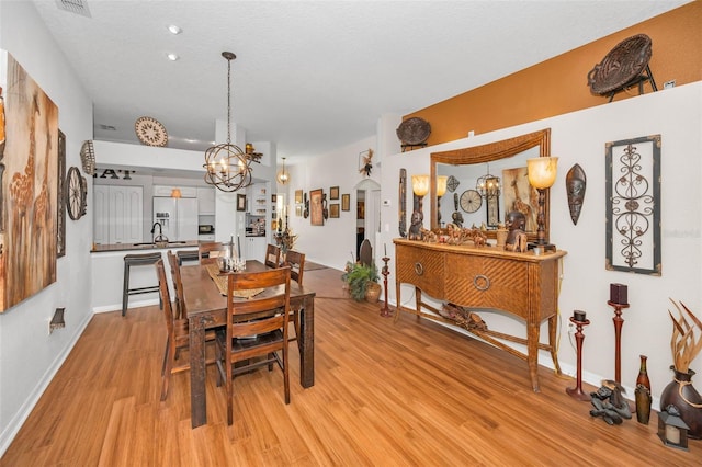 dining room featuring arched walkways, light wood finished floors, a chandelier, and baseboards