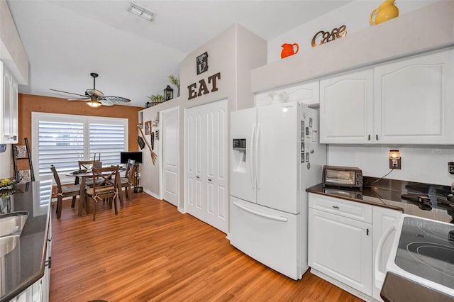 kitchen featuring electric range oven, white refrigerator with ice dispenser, visible vents, and white cabinetry