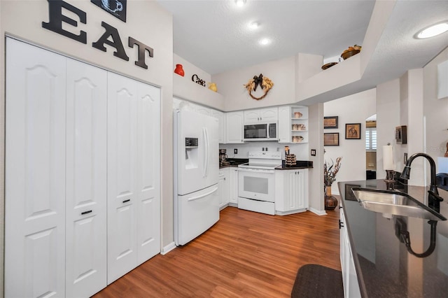 kitchen featuring white appliances, wood finished floors, a sink, white cabinets, and dark countertops