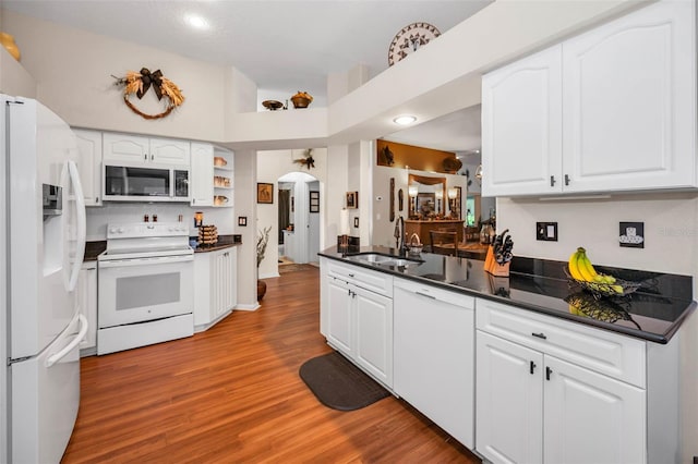 kitchen featuring arched walkways, white appliances, dark countertops, and a sink