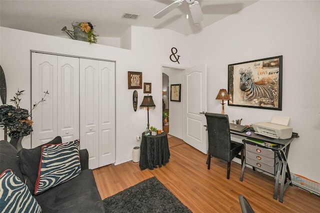 home office featuring lofted ceiling, a ceiling fan, visible vents, and wood finished floors