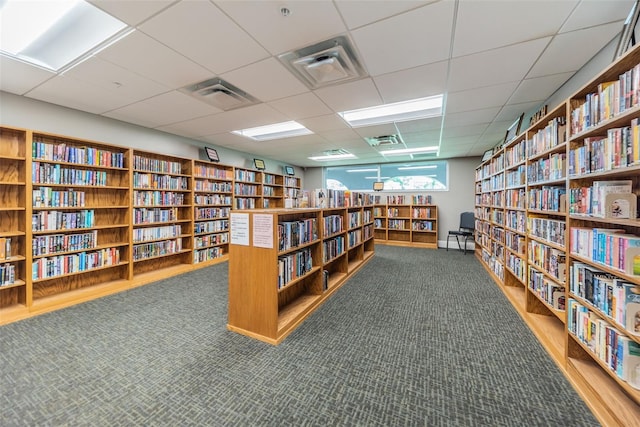 living area with a paneled ceiling, visible vents, and wall of books