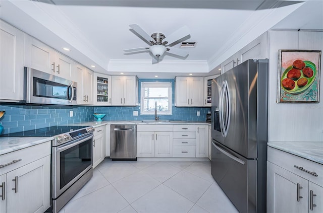 kitchen with stainless steel appliances, a sink, ornamental molding, a tray ceiling, and glass insert cabinets