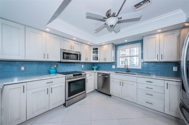 kitchen with a raised ceiling, glass insert cabinets, stainless steel appliances, light countertops, and a sink