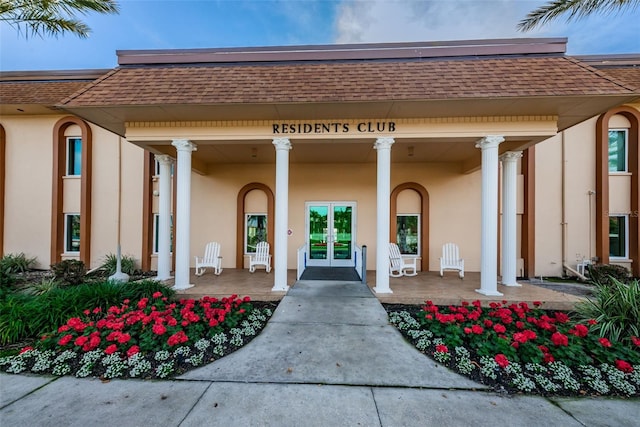 doorway to property featuring covered porch, french doors, a shingled roof, and stucco siding