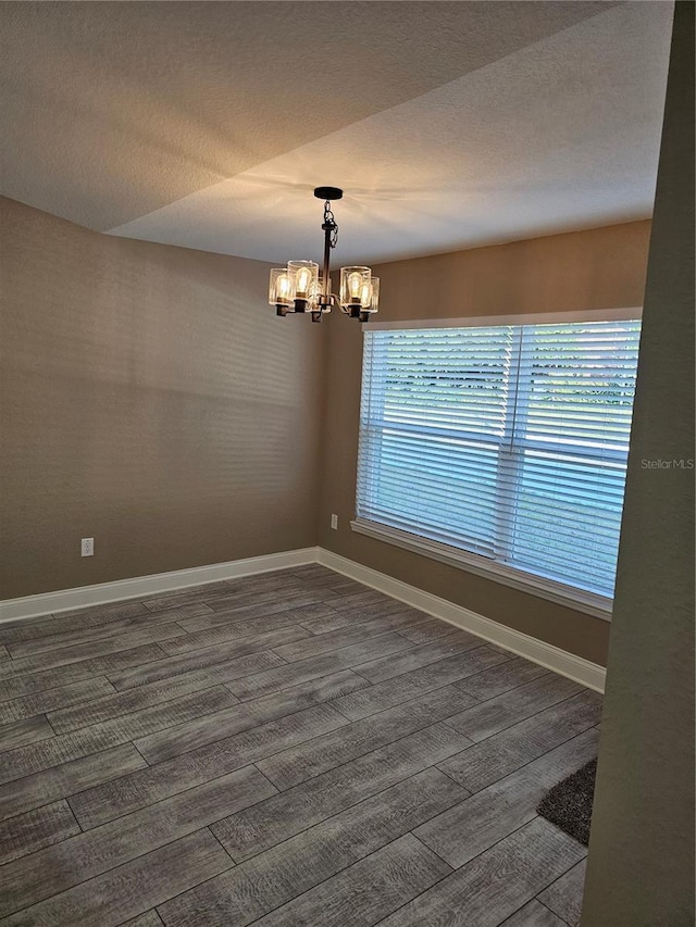 empty room with dark hardwood / wood-style flooring, a textured ceiling, and a chandelier