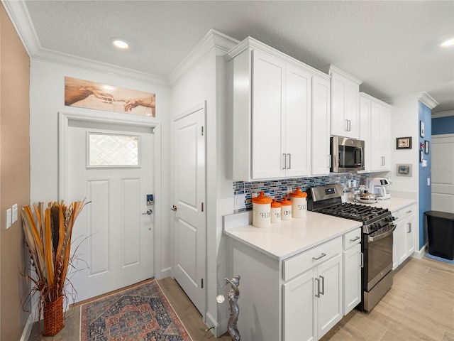 kitchen featuring light hardwood / wood-style flooring, white cabinetry, stainless steel appliances, tasteful backsplash, and ornamental molding