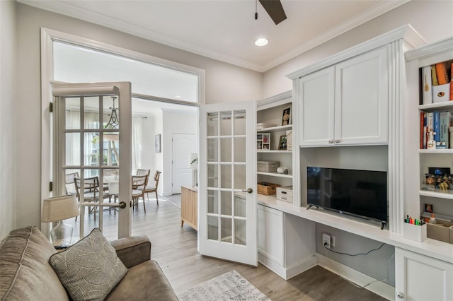 living room with ornamental molding, built in desk, ceiling fan, and light hardwood / wood-style flooring