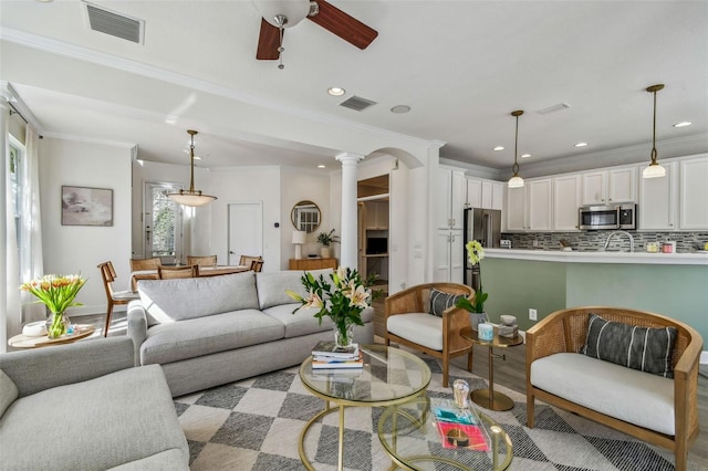 living room with decorative columns, ornamental molding, ceiling fan, and light hardwood / wood-style flooring