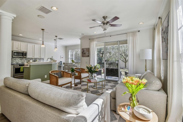 living room featuring decorative columns, crown molding, and ceiling fan