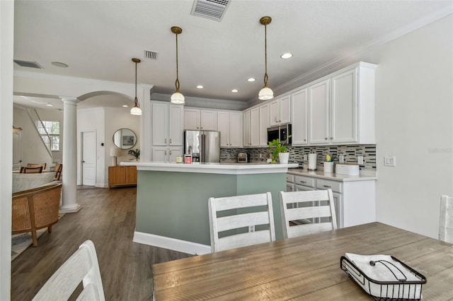 kitchen featuring stainless steel appliances, decorative columns, hanging light fixtures, and white cabinets