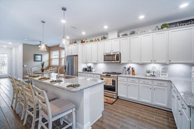 kitchen with hanging light fixtures, an island with sink, appliances with stainless steel finishes, and white cabinetry