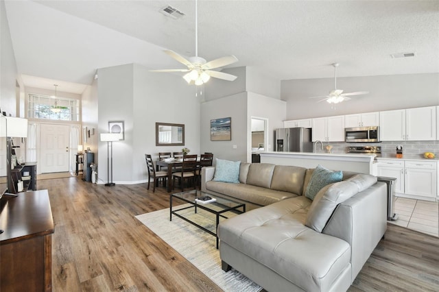 living room with sink, ceiling fan, hardwood / wood-style floors, high vaulted ceiling, and a textured ceiling