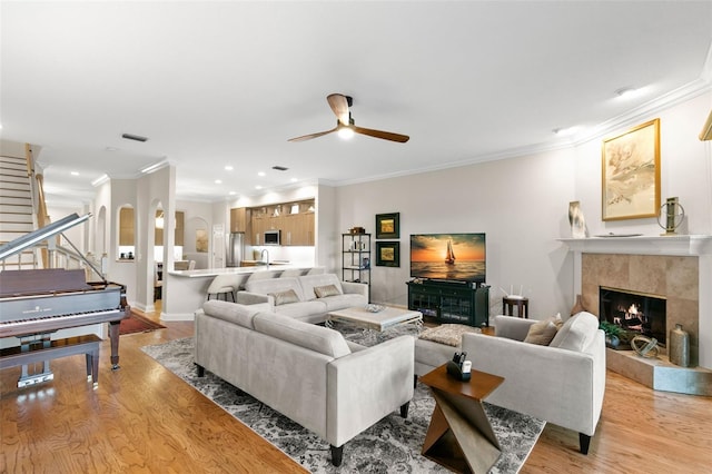 living room featuring ceiling fan, ornamental molding, a fireplace, and light hardwood / wood-style floors