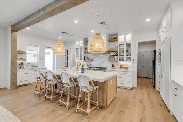 kitchen featuring premium range hood, white cabinetry, a center island with sink, beamed ceiling, and light hardwood / wood-style floors