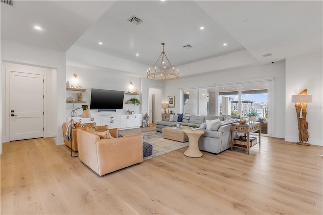 living room with an inviting chandelier, a tray ceiling, and light hardwood / wood-style floors