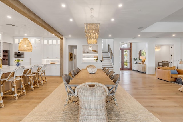 dining room featuring an inviting chandelier, light hardwood / wood-style flooring, and beamed ceiling