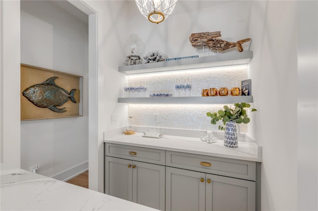 bar featuring light stone counters and gray cabinetry