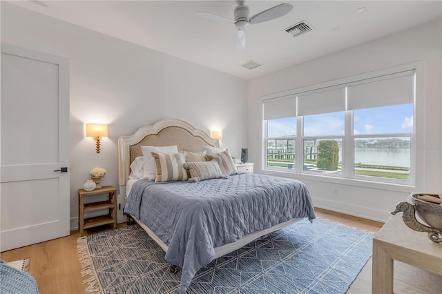 bedroom featuring a water view, hardwood / wood-style floors, and ceiling fan