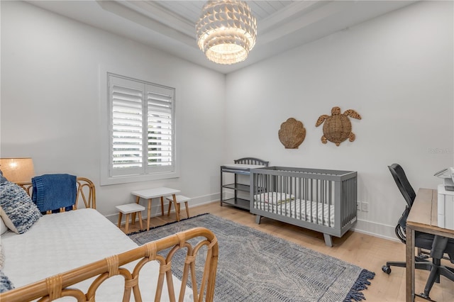 bedroom with a tray ceiling, light wood-type flooring, and a notable chandelier