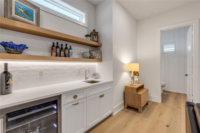 bar with sink, white cabinetry, wine cooler, tasteful backsplash, and light hardwood / wood-style floors