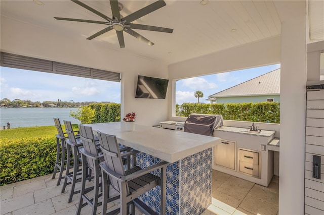 view of patio with an outdoor kitchen, a wet bar, a water view, ceiling fan, and a grill