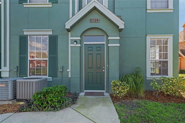 doorway to property with stucco siding and central AC unit