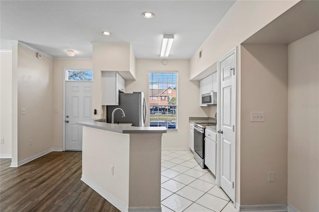 kitchen with white cabinetry, a peninsula, stainless steel appliances, and baseboards