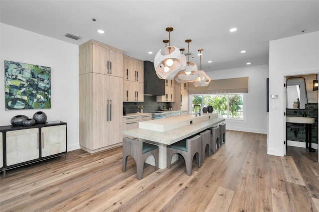 kitchen with a center island with sink, decorative backsplash, a kitchen bar, decorative light fixtures, and light brown cabinets