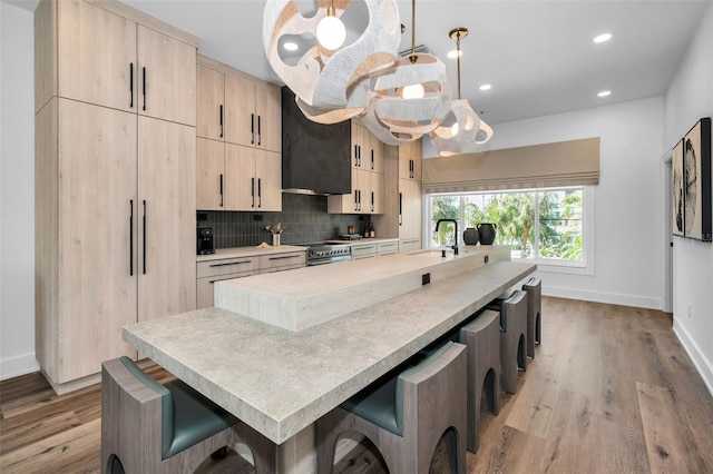 kitchen with exhaust hood, hanging light fixtures, light brown cabinets, a kitchen island, and backsplash