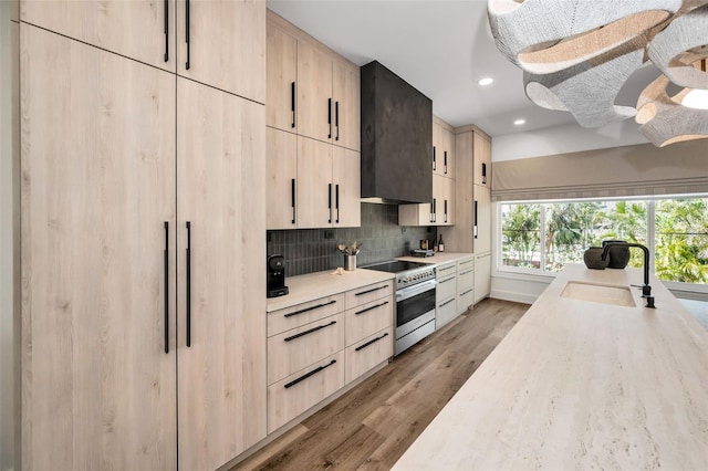 kitchen featuring light brown cabinetry, sink, wall chimney range hood, and high end stainless steel range oven