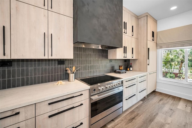 kitchen with light brown cabinetry, decorative backsplash, custom range hood, light wood-type flooring, and stainless steel electric range