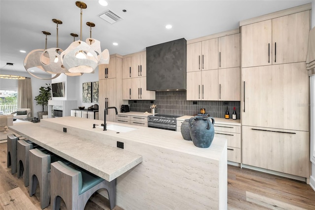 kitchen with pendant lighting, sink, tasteful backsplash, a kitchen bar, and light brown cabinetry