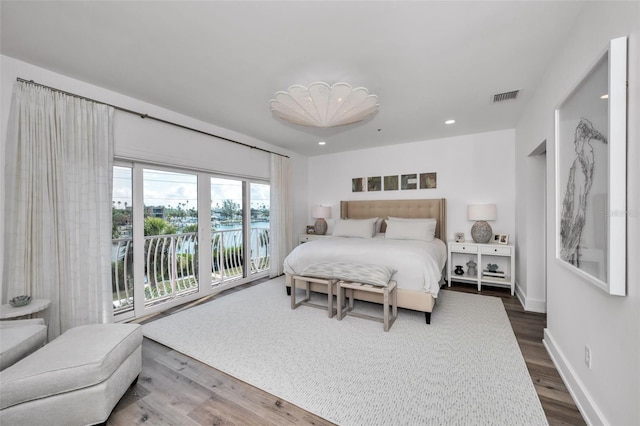 bedroom with hardwood / wood-style flooring, a water view, and access to outside