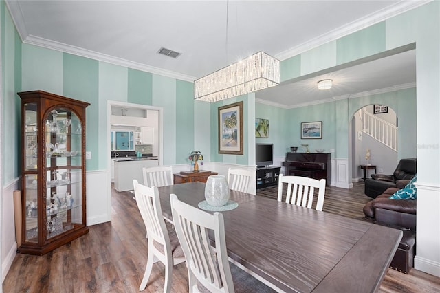 dining room with visible vents, crown molding, arched walkways, wood finished floors, and a notable chandelier