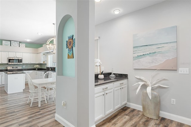 bar featuring backsplash, a sink, a notable chandelier, light wood-style floors, and stainless steel appliances