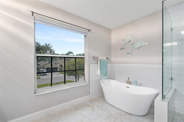 bathroom with baseboards, a wealth of natural light, tiled shower, and a soaking tub