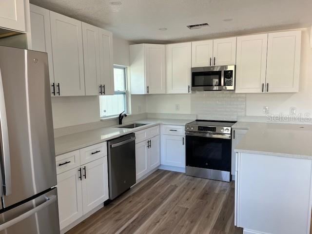 kitchen with sink, tasteful backsplash, appliances with stainless steel finishes, hardwood / wood-style floors, and white cabinets