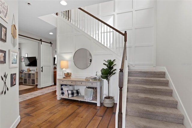 staircase with hardwood / wood-style flooring, a barn door, and a high ceiling