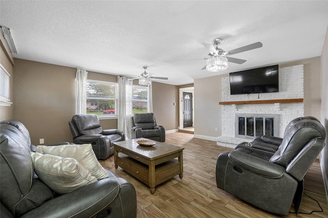 living room with hardwood / wood-style flooring, ceiling fan, a brick fireplace, and a textured ceiling