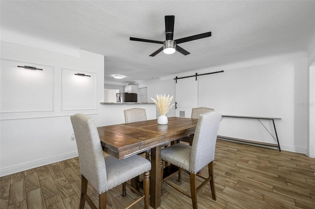 dining space with ceiling fan, dark wood-type flooring, a barn door, and a textured ceiling