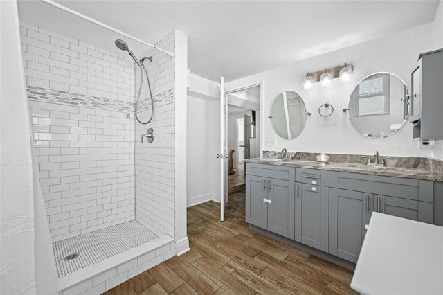 bathroom with wood-type flooring, tiled shower, and vanity