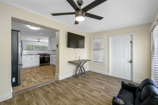 living room with ceiling fan, a textured ceiling, and light wood-type flooring