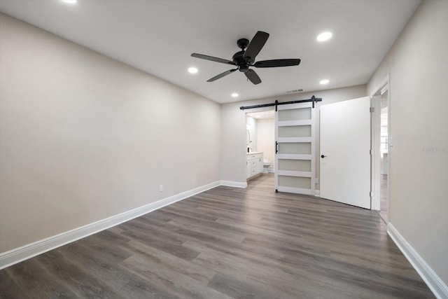 unfurnished bedroom featuring ceiling fan, a barn door, connected bathroom, and dark hardwood / wood-style flooring