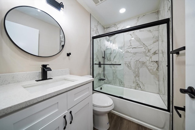 full bathroom featuring hardwood / wood-style flooring, bath / shower combo with glass door, vanity, and toilet