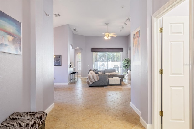 hall featuring baseboards, visible vents, arched walkways, track lighting, and light tile patterned flooring