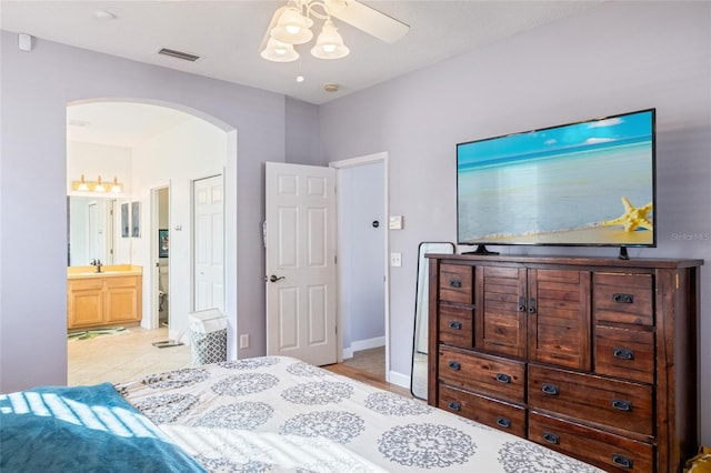 bedroom featuring arched walkways, ceiling fan, ensuite bathroom, a sink, and visible vents