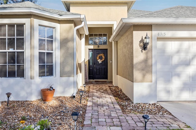 view of exterior entry featuring a garage, roof with shingles, and stucco siding